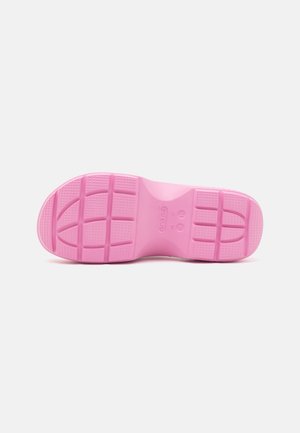 Semelle de chaussure en caoutchouc rose avec motif de grip texturé et marquages de la marque visibles sur fond blanc.