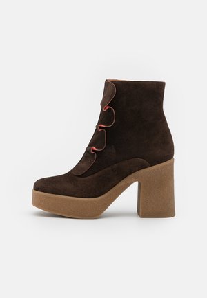 Bota de ante marrón oscuro hasta el tobillo con tacón grueso tipo plataforma en beige y detalles en forma de solapa con bordes en rosa en la parte delantera.