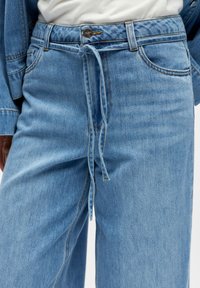 Gaiši zili džinsa bikses ar elastīgu vidukļa joslu un regulējamu aukliņu. Aprīkotas ar parastajām priekšējām kabatām un kontrastējošām šuvēm.