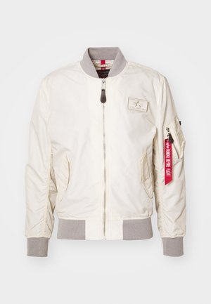 Chaqueta bomber de color beige claro hecha de nailon, con puños acanalados y un cuello gris. Cierre de cremallera con un bolsillo lateral y detalle de etiqueta roja.