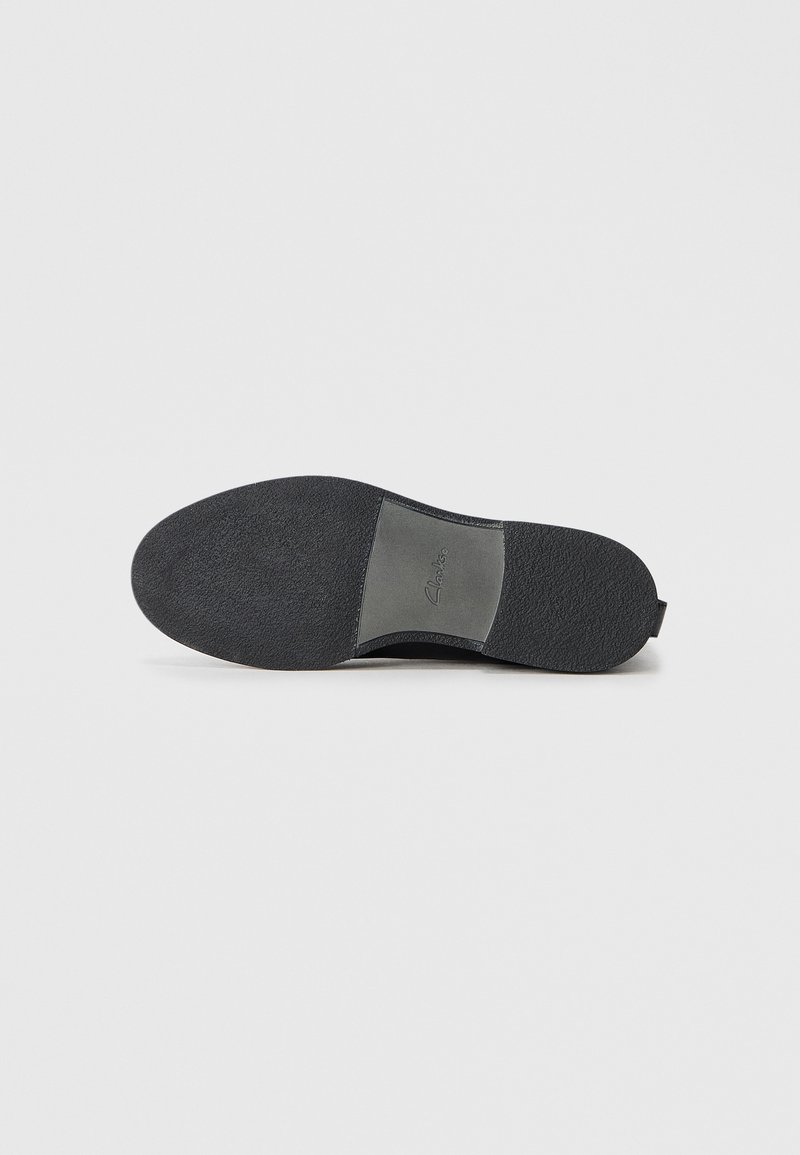 Schwarze Schuhsohle mit strukturierten Oberflächen, die einen glatten grauen Akzentbereich aufweist. Flaches Design mit abgerundetem Zeh und minimalem Markenlogo.
