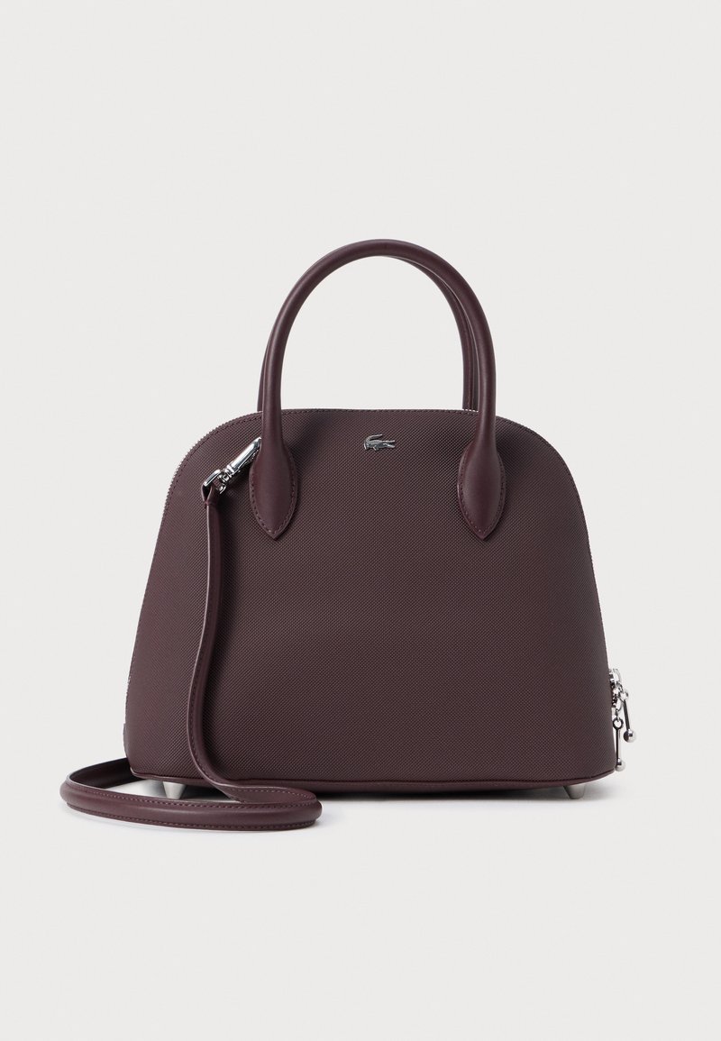 Bordeaux geklede handtas met dubbele handgrepen, een afneembare schouderriem en zilverkleurige hardware. Bevat een ritssluiting en een merklogo-detail.