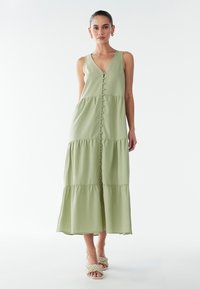 Lichtgroene, mouwloze maxi-jurk met een V-hals, gelaagde rok en knopen aan de voorkant. Gemaakt van een gladde stof. Geen zichtbare patronen.