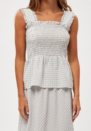 Femme portant un haut smocké sans manches à carreaux blancs et gris avec des bretelles à volants et une jupe assortie.