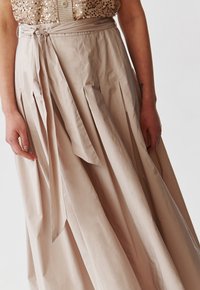 Beige pleated skirt made of smooth fabric, featuring a tied waistband and a flowing design, with visible texture and soft sheen.