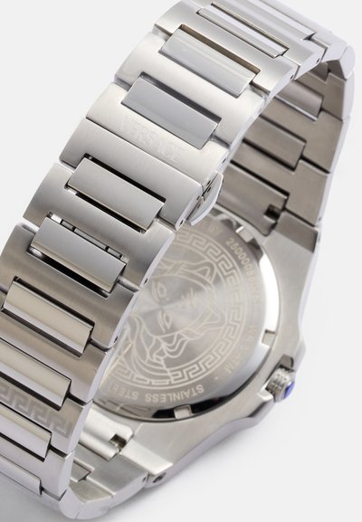 Reloj de acero inoxidable con un acabado pulido y cepillado. Presenta una pulsera de eslabones geométricos, fondo grabado y un acento azul en la corona.