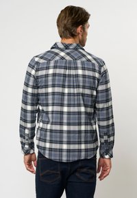 Patikrinama marškiniai su mėlynos, pilkos ir baltos plaidų raštais bei oranžiniais akcentais. Pagaminti iš audinio, turi klasikinį apykaklę ir sagų rankoves.