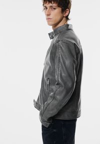 Grå læderjakke med en tætsiddende pasform, der har lynlåslommer, trykknapkrave og en subtil tekstur. Båret med mørke denim.