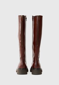 Braune Lederstiefel in Kniefhöhe mit glatter Textur, seitlichen Reißverschlüssen und einem massiven schwarzen Absatz. Besitzen ein tailliertes Design und minimale Hardware.