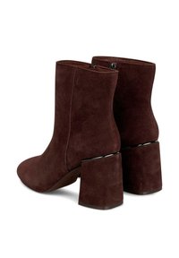 Botas de tobillo de ante marrón con una forma recta, que presentan un tacón grueso y un acento negro en la base del tacón. Cierre con cremallera lateral.