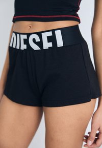 Calças curtas pretas com uma cintura elástica larga, apresentando o texto branco "DIESEL". Feitas de um tecido suave, com um corte descontraído e bordas limpas.