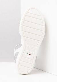 Semelle de sandale blanche avec des rainures texturées, affichant le logo 'NG' et le texte 'FABRIQUÉ EN ITALIE', rehaussée par le drapeau italien rouge et vert.