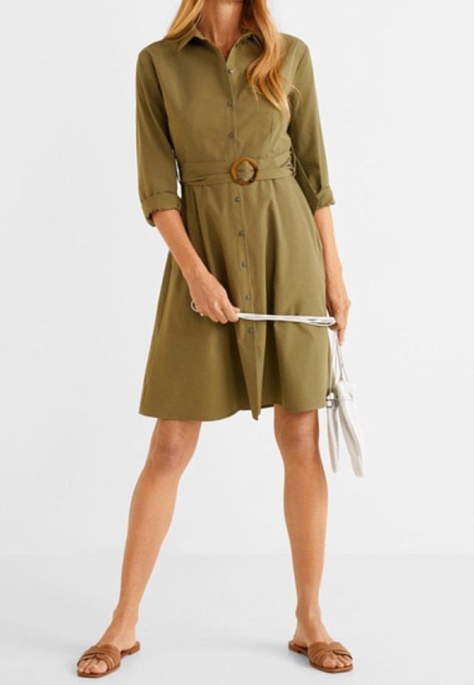 Femme portant une robe boutonnée vert olive avec une ceinture assortie, tenant un sac à main blanc et portant des sandales plates marron.