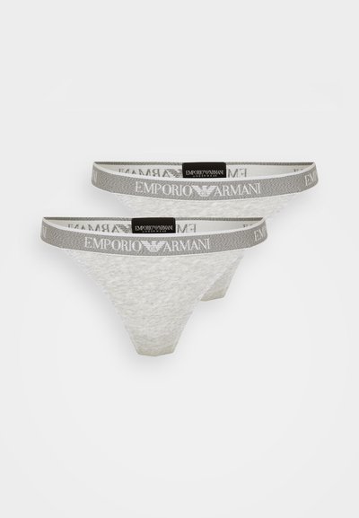 Deux strings en dentelle blanche avec une ceinture élastique grise portant le logo "Emporio Armani". Texture douce et transparente avec un design classique.