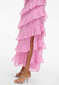 Rosa volangklänning med lager av chiffon, med en hög slits. Åtföljs av silverfärgade högklackade sandaler med remmar.