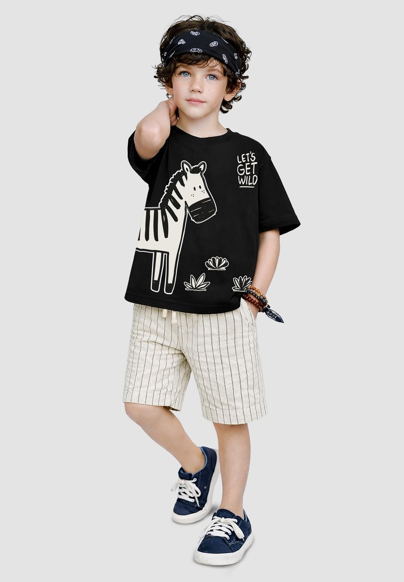 Dreng med krøllet hår iført sort bandana, sort T-shirt med en zebra og teksten "Let's Get Wild", stribede shorts og marineblå sneakers.
