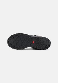 Terränglöpningssula, svart gummi med djupa mönstrade piggar, strukturerat mönster, framträdande röd accent, hållbar konstruktion för grepp på varierad terräng.