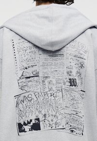 Ανοιχτό γκρι φούτερ με κουκούλα, με μαύρη κολάζ σχεδίασης στυλ σκίτσου που περιλαμβάνει χειρόγραφες σημειώσεις, σχέδια και αφηρημένο κείμενο στην πλάτη.