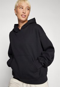 Felpa nera con cappuccio, dotata di tasca anteriore, vestibilità comoda, polsini e orlo a coste. Realizzata in tessuto morbido e strutturato, adatta per un abbigliamento casual.