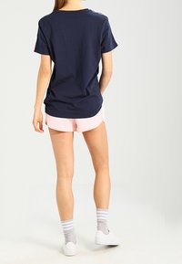 Marineblauwe katoenen t-shirt met een relaxte pasvorm, gecombineerd met lichtroze shorts. Het model draagt grijsgestreepte sokken en witte sneakers.