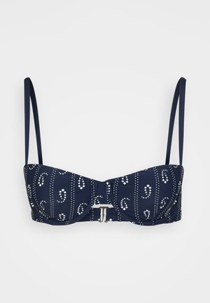 Donkerblauwe bikinibovenkant met witte stippen en bloemenpatronen, voorzien van beugelcups, verstelbare bandjes en een metalen sluiting.