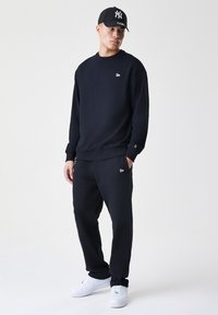 Sort sweatshirts og joggers lavet af en blanding af bomuldsstof. Har en rund halsudskæring, elastiske manchetter og broderede logo-detaljer. Hvide sneakers.