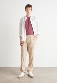 Lett hvit skjorte over en kastanjestrukturert skjorte, kombinert med beige bukser med elastisk liv og hvite joggesko med gummisåler.