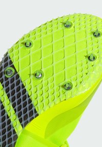 Bright yellow athletic shoe sole featuring a textured grip pattern, metal studs for traction, and a smooth, durable surface design.