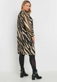 Pitkä, läpinäkyvä mekko musta-tan-raidallisella seeprahauksen kuviolla; siinä on pitkät puffihihat, rento malli ja suora helma. Yhdistetty mustiin nilkkureihin.