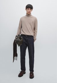 Beige high-neck sweater, dark denim jeans, brown leather shoes, and a green bag. The outfit includes a dark brown scarf with fringe.