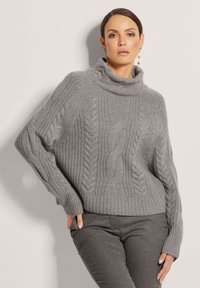Grauer Strickpullover mit hohem Rollkragen und strukturierten Zopfmustern. Verfügt über gerippte Bündchen und Saum, kombiniert mit dunkelgrauen, eng anliegenden Hosen.
