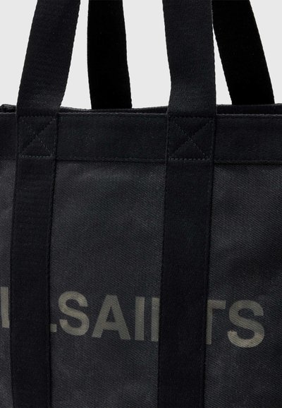 Sac cabas en tissu noir avec des poignées épaisses noires et un texte gris partiellement visible "SAINTS" à l'avant.