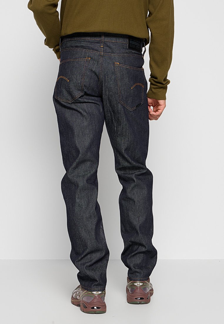 Dunkelblaue Jeans im geraden Schnitt mit aufgesetzten Gesäßtaschen und braunen Nähten, getragen mit hellbraunen Wanderschuhen.