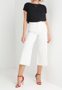 Svart kortärmad topp med spetsdetalj, tillsammans med vitrandiga vida byxor och röda högklackade sandaler.