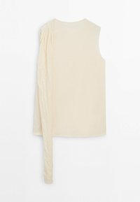 Haut beige sans manches avec un seul panneau long en tissu texturé drapé sur l'épaule gauche et tombant au-delà de l'ourlet.