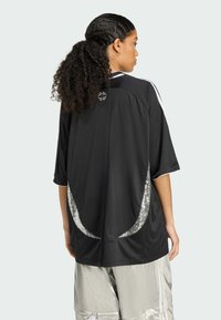 Čierny športový dres s krátkymi rukávmi, voľným strihom, striebornými akcentmi pri leme a okrúhlym logom v oblasti zadného krku.