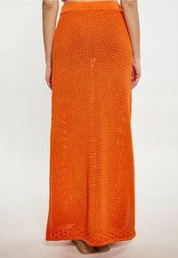 Gebreide maxirok in fel oranje, met een opengewerkt ontwerp en een aansluitende tailleband. De lengte reikt tot de enkels met een tekstuurfinish.