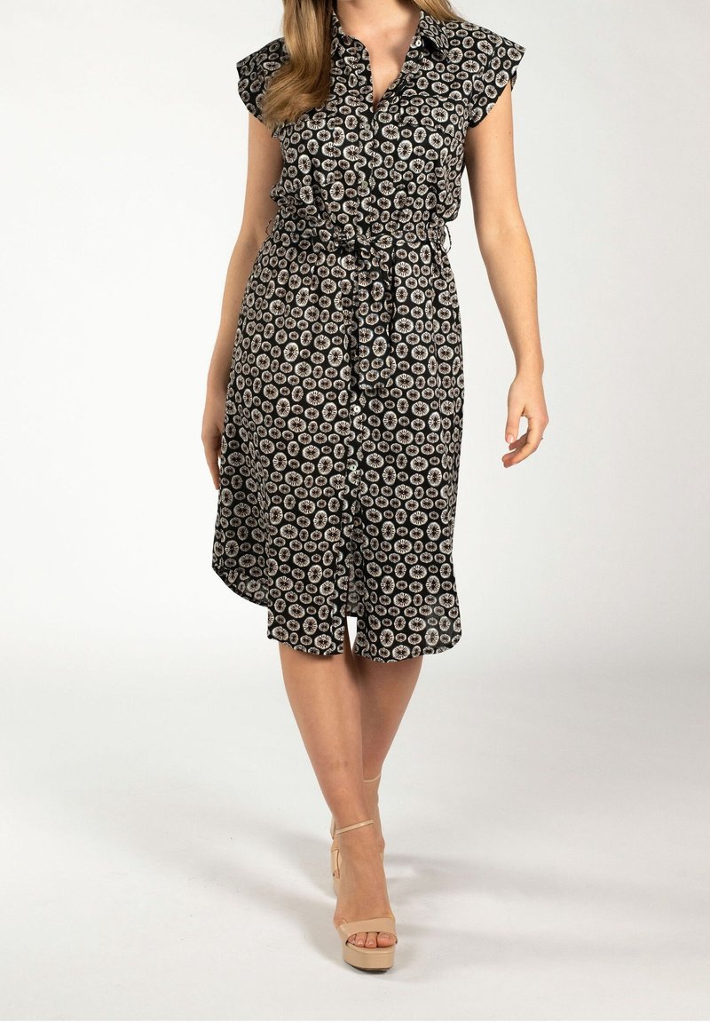 Abito a righe bianco e nero con maniche corte a volant, vita stretta e orlo al ginocchio. Indossato con sandali beige con tacco.