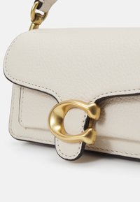 Borsa a mano in pelle beige chiaro con una superficie testurizzata, presenta una chiusura in tono oro e una cucitura scura a contrasto lungo i bordi.