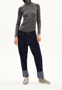 Pantalones de mezclilla azul oscuro con dobladillos enrollados, combinados con un suéter gris acanalado con un cuello alto y cierre plateado. Zapatos con patrón de cebra.