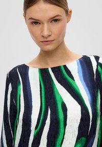 Mehrfarbiges Oberteil mit weitem Bootsausschnitt. Das Design umfasst kräftige grüne, blaue und schwarze Streifen auf einem weißen Grund und hat eine glatte Textur.