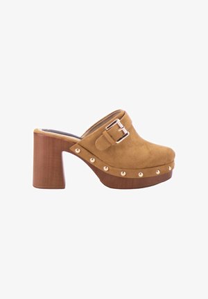 Zueco de ante marrón con tacón grueso de madera, correa con hebilla en la parte superior y tachuelas metálicas a lo largo del borde de la suela.