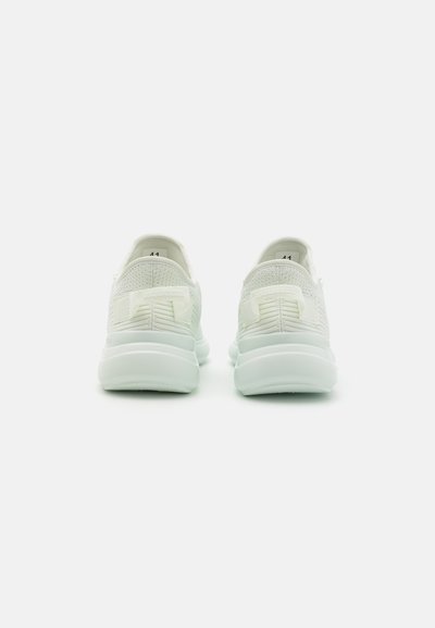 Scarpe sportive bianche con tomaia in maglia testurizzata, suola in gomma liscia e dettaglio del logo sul tallone. L'etichetta della taglia mostra "41" all'interno.