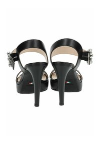 Sandales à talons hauts noires avec une finition en cuir lisse, dos ouvert, sangle de cheville et accents décoratifs en argent près du talon.