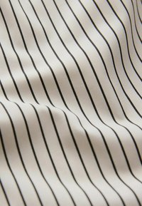 Tissu blanc avec des fines rayures verticales noires espacées régulièrement, présenté avec des plis doux créant de légères ombres et reflets.