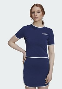 Marindress med korta ärmar, vit kant och logotypdetalj. Tätt sittande topp som övergår i en utsvängd kjol, tillverkad av ett mjukt tyg.