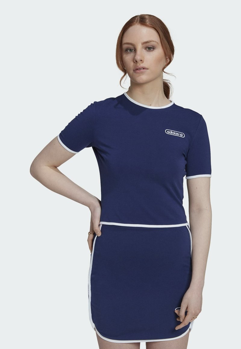 Marindress med korta ärmar, vit kant och logotypdetalj. Tätt sittande topp som övergår i en utsvängd kjol, tillverkad av ett mjukt tyg.