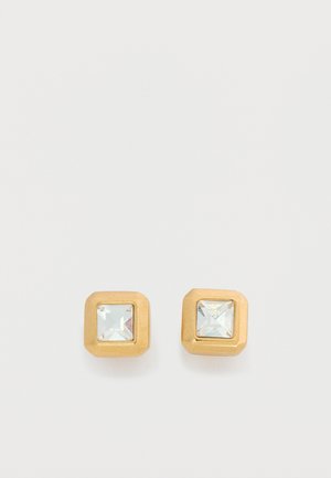 Square-cut clear gemstones set in small gold metal stud earrings on a light background.