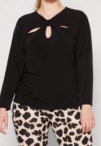 Top nero a maniche lunghe con un design frontale attorcigliato e aperture a chiave. Realizzato in tessuto morbido, abbinato a leggings con stampa leopardata.
