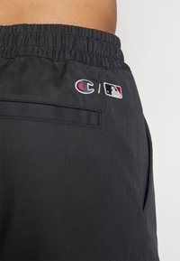 Pantalones cortos deportivos negros con cintura elástica, que cuentan con logotipos bordados de Champion y MLB en la parte posterior. Textura suave con bolsillos laterales.
